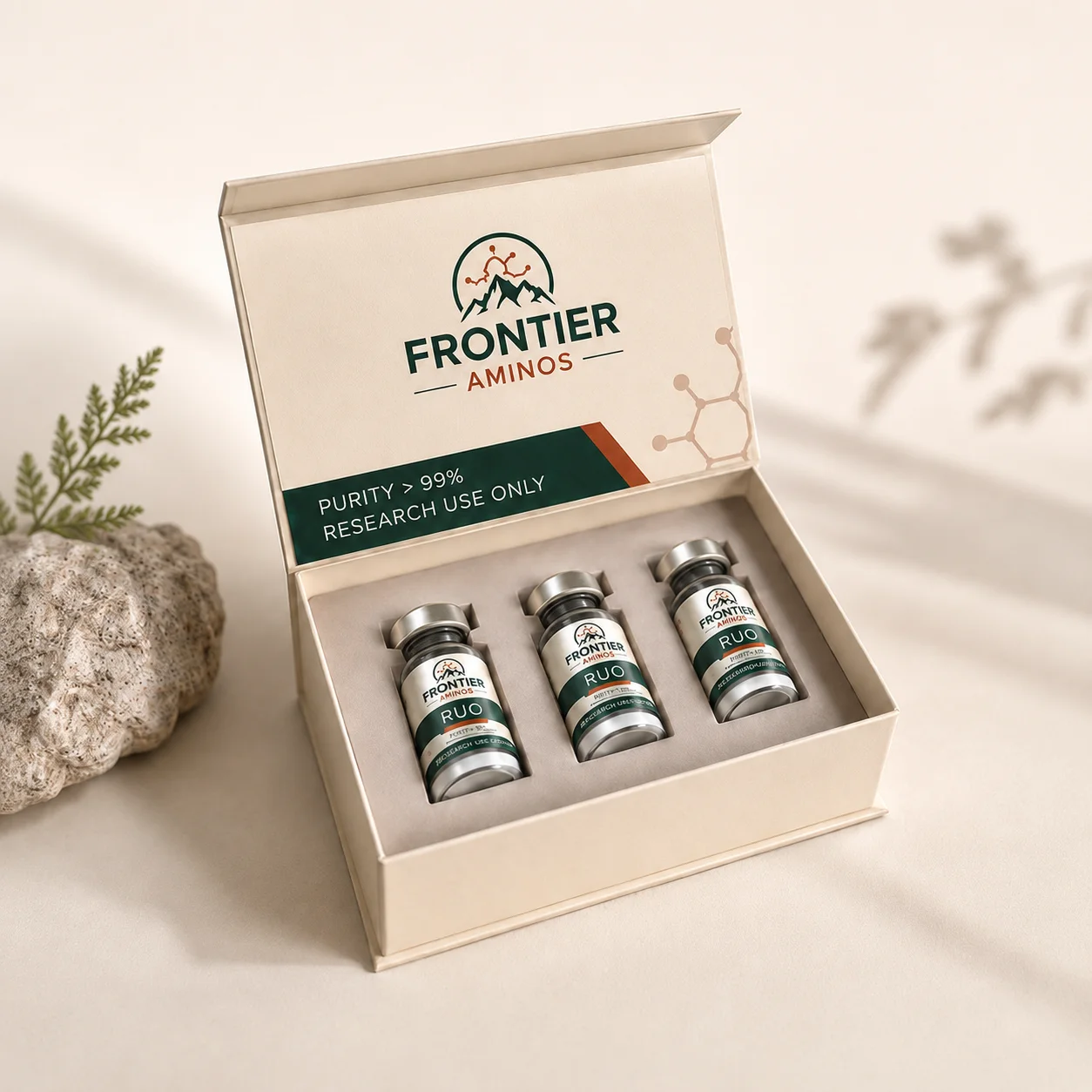 Frontier Aminos three-vial field kit, open on a cream ground beside a sprig of foliage and a pale stone